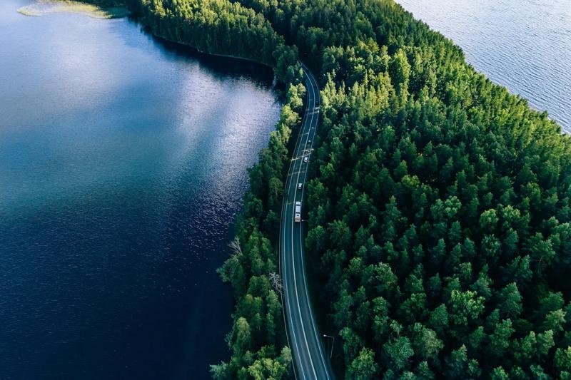 Aerial view of road in green woods and blue lakes water in summer Finland