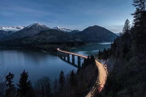 Car trails of the last people heading home from their hike and driving over the bridge at Lake Sylvenstein, upper Bavaria, Germany.