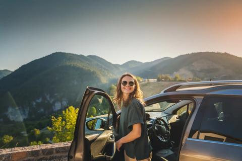 Smiling woman traveling by car in the mountains taking a break on the side of the road
