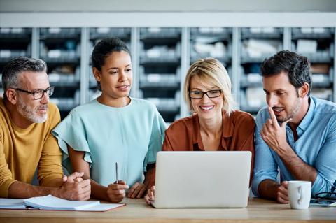 Smiling businesswoman using laptop with colleagues. Male and female executives are working together. They arte wearing smart casuals at textile industry.
