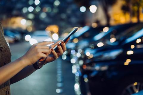 Cropped shot of a woman's hand using smartphone while walking to her car in car park in city at night